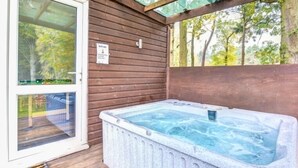 A hot tub in a wooden cabin with a glass door and a view of trees. - Warren Cottage (Norwich)
