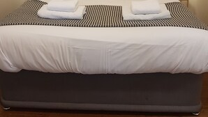 A neatly made bed with white linens, two gray pillows, and a striped blanket. There are two bedside lamps on either side of the bed. - Warren Cottage (Norwich)