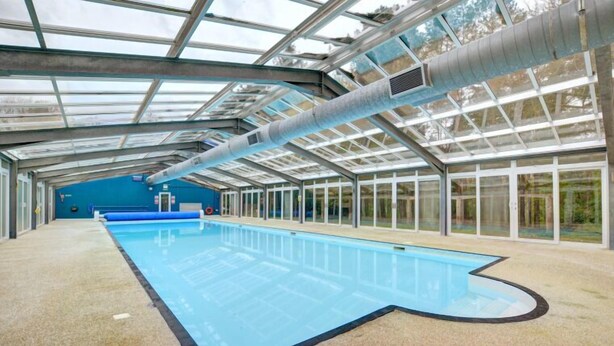 An indoor swimming pool with a glass ceiling and a blue wall in the background. - Warren Cottage (Norwich)