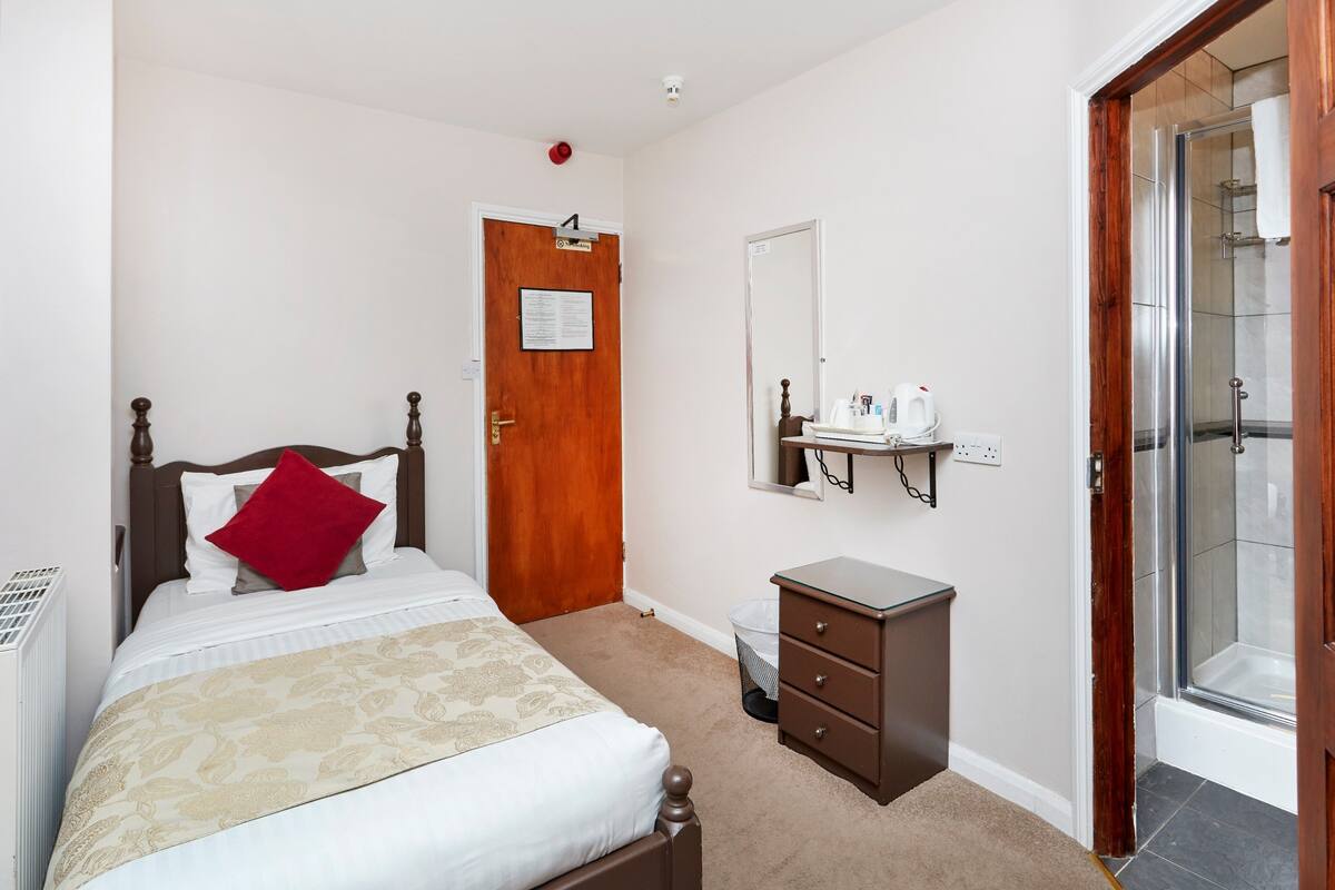 Ein Schlafzimmer mit einem Bett, einer Holztür, einem kleinen Schminktisch, einem Spiegel und einer Dusche.