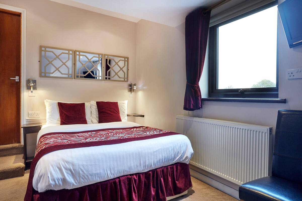 Ein Hotelzimmer mit Bett, einem Vorhangfenster, einem Heizkörper und einem Sessel.