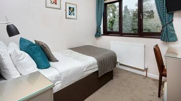 A bedroom with a bed, bedside table, lamp, and a window with curtains.