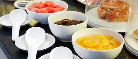 A table with various food items including bowls of fruit and pastries, and white ceramic dishes with spoons.