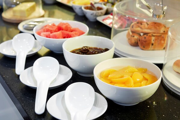 A table with various food items including bowls of fruit and pastries, and white ceramic dishes with spoons. - Conifers Guest House (Oxford)