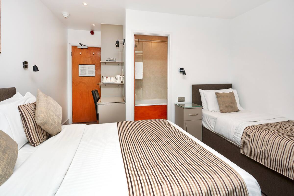 Ein Hotelzimmer mit zwei Betten, einem Schreibtisch, einem Stuhl, einem Kleiderschrank und einem kleinen Schrank.