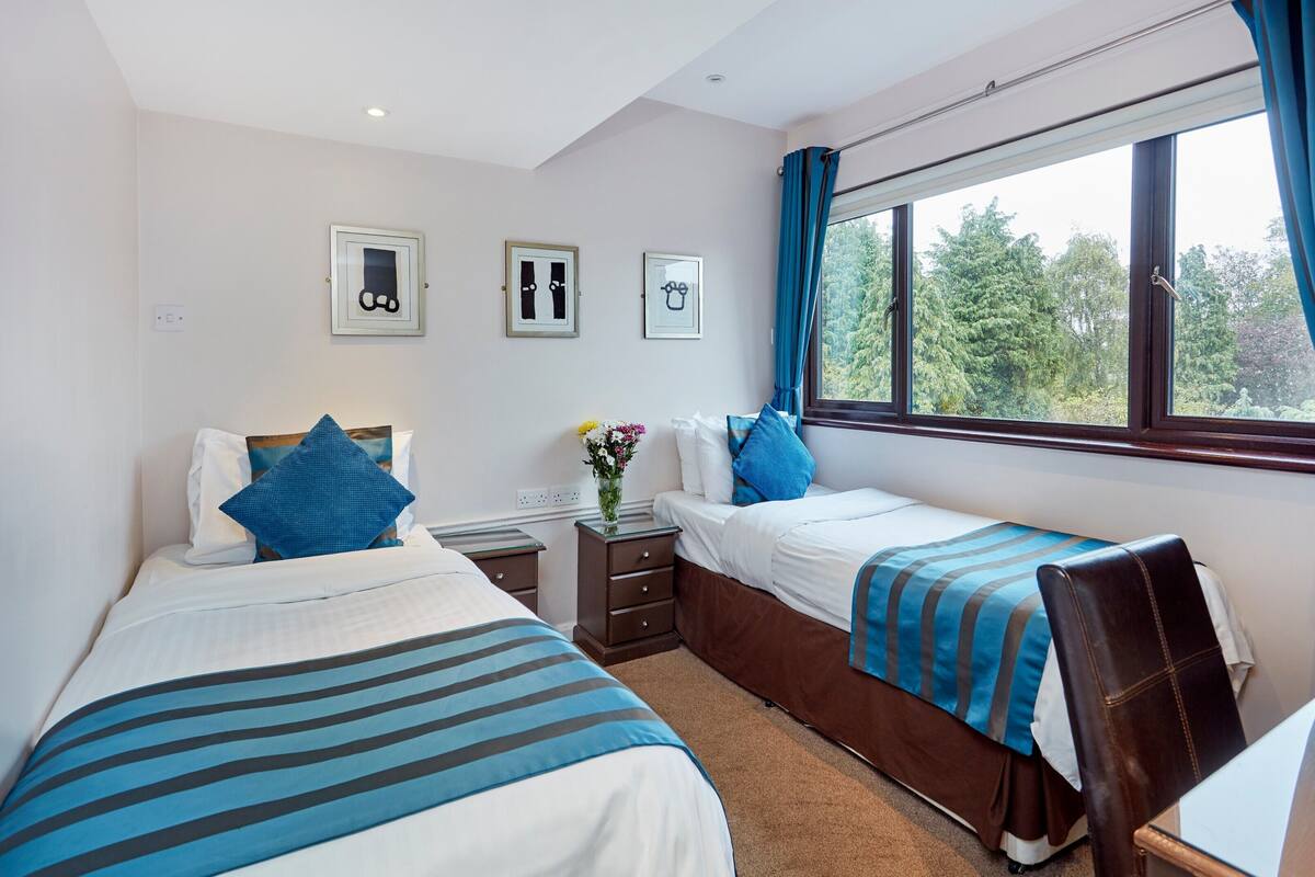 Ein Hotelzimmer mit zwei Betten, einem Schreibtisch und einem Fenster mit Vorhängen.
