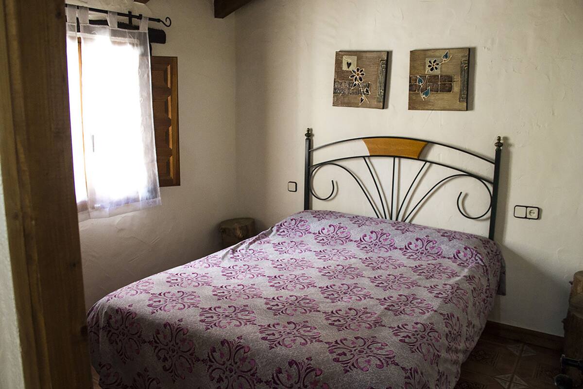 A bedroom with a bed, a window with a curtain, and two wall-mounted artworks.