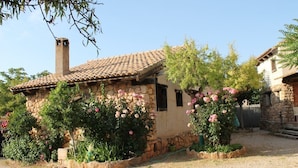Une maison en pierre avec un toit de tuiles, entourée de gravier et de plantes en fleurs.