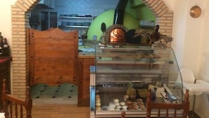 Un intérieur rustique avec une arche en briques menant à un espace cuisine, une vitrine contenant des produits alimentaires et un appareil électroménager vert.