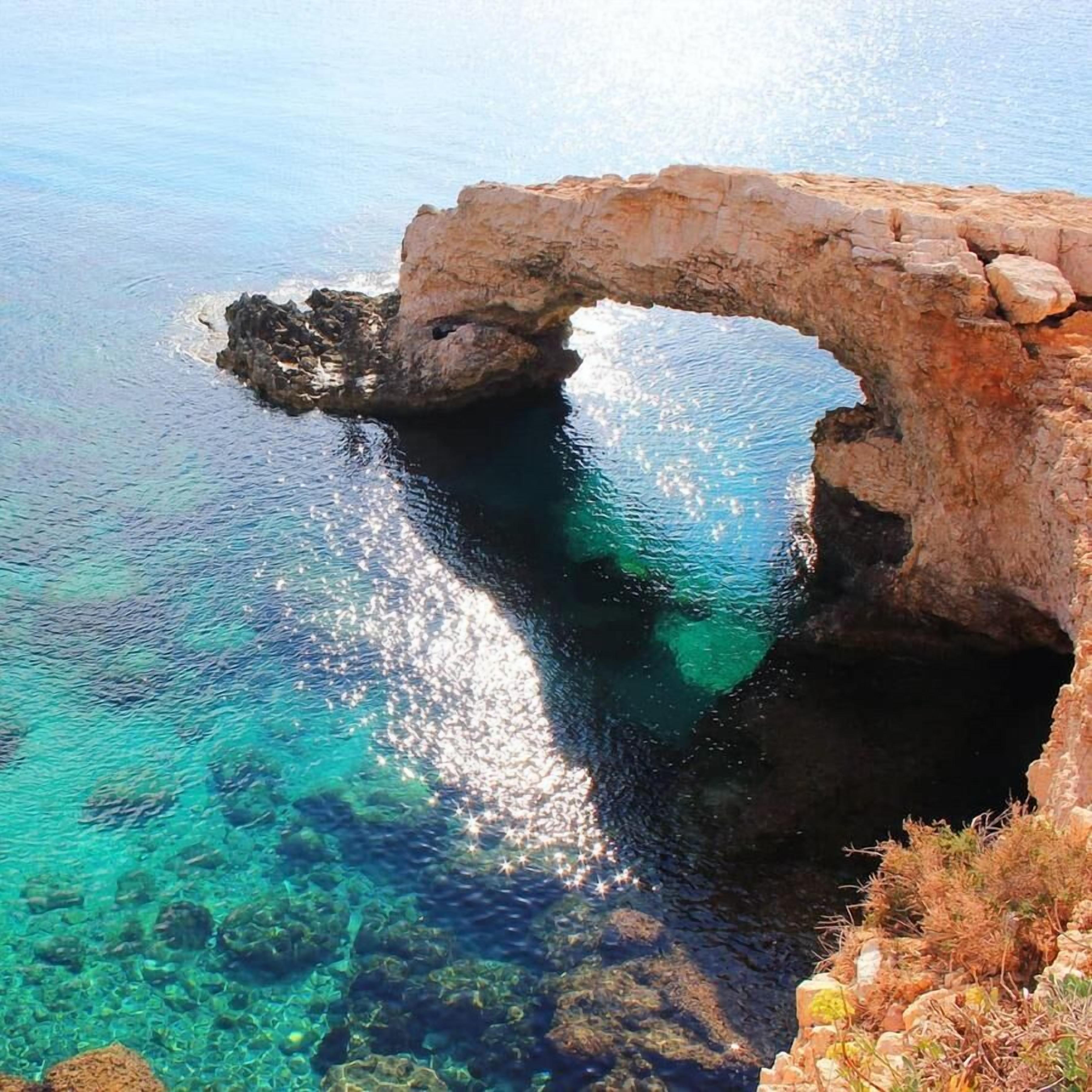 Un arco naturale di roccia su acque cristalline blu, con rocce visibili sott'acqua e vita marina.