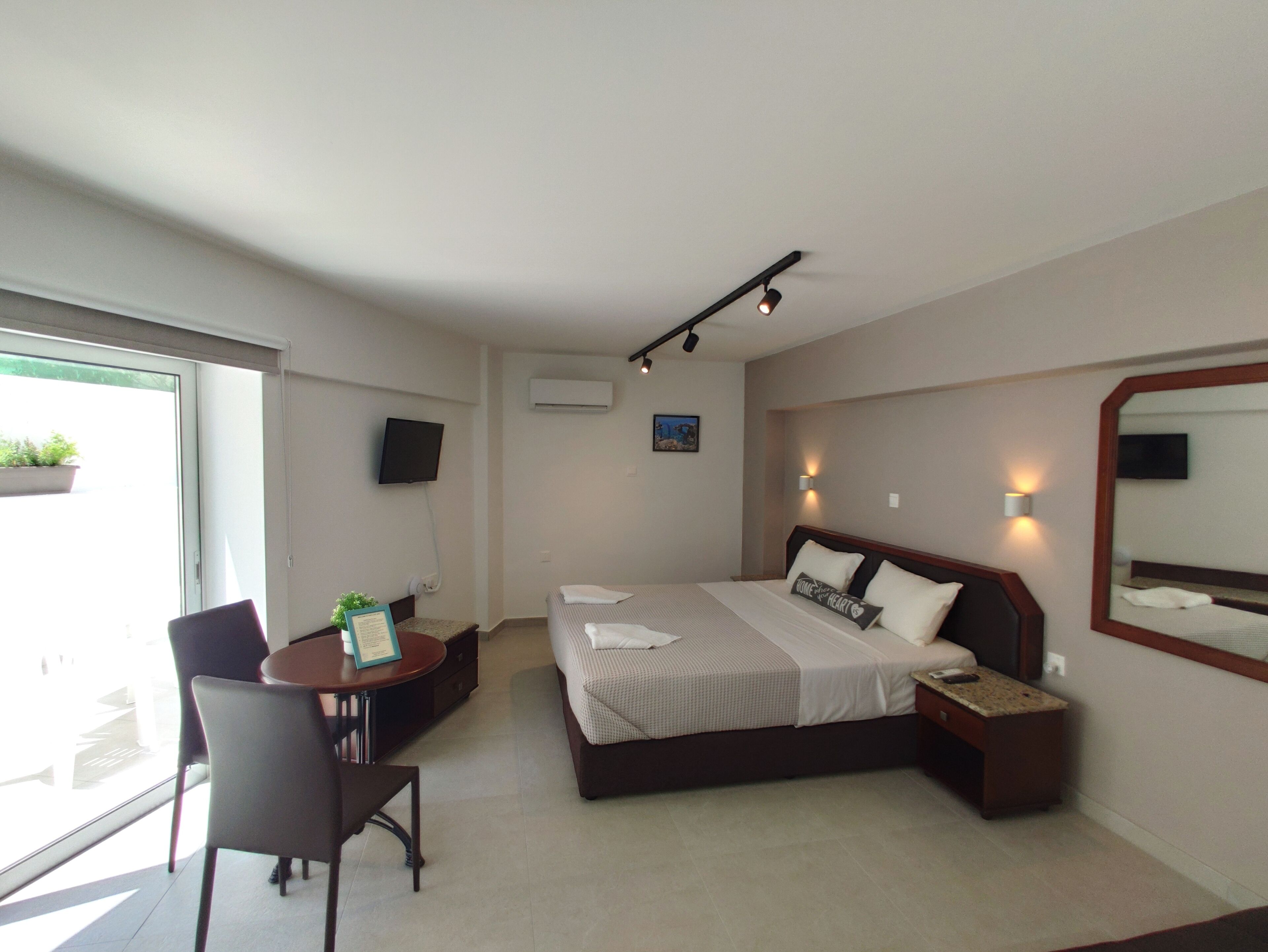 Una habitación de hotel moderna con cama, mesita de noche, silla, escritorio y un amplio ventanal.