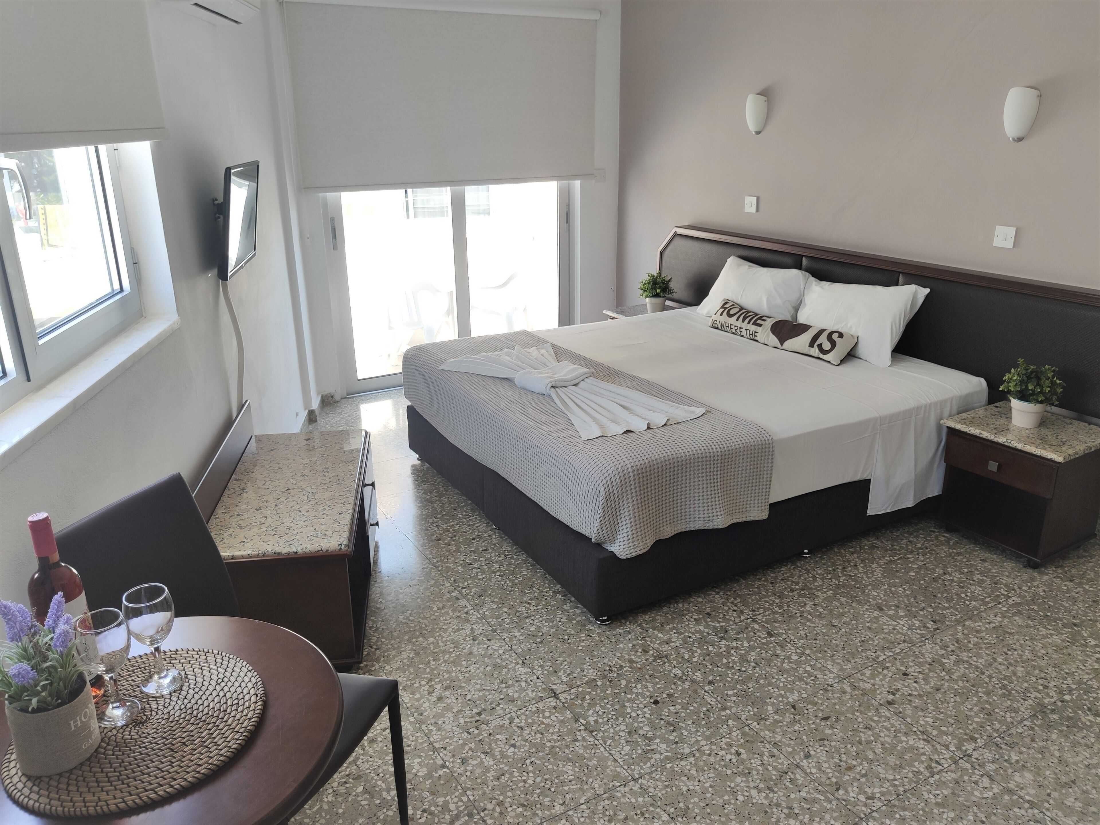 Un dormitorio moderno con una cama grande, una mesita de noche con una planta y una ventana que proporciona luz natural.