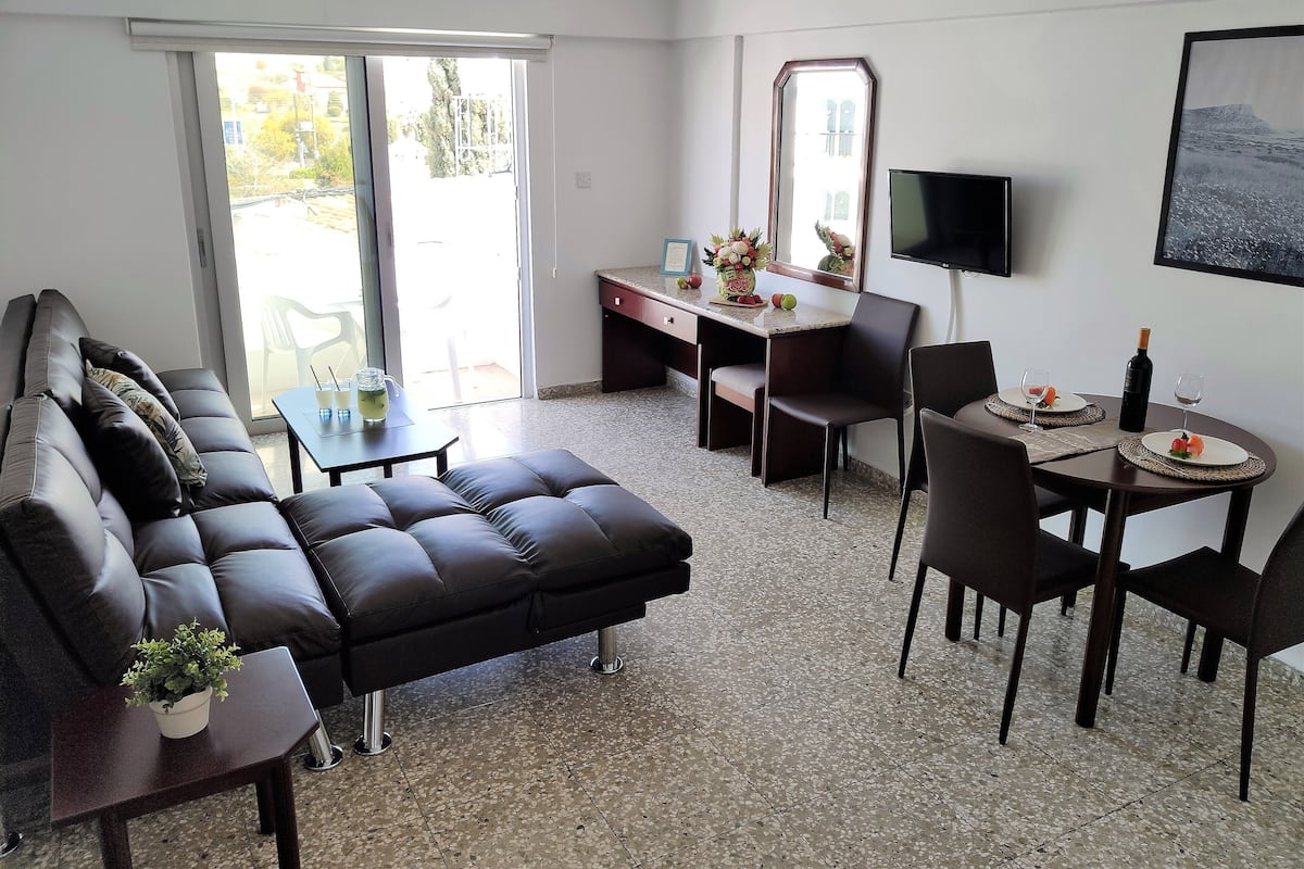 Una sala de estar moderna con un sofá, una mesa de comedor con sillas, un escritorio pequeño y un televisor montado en la pared.