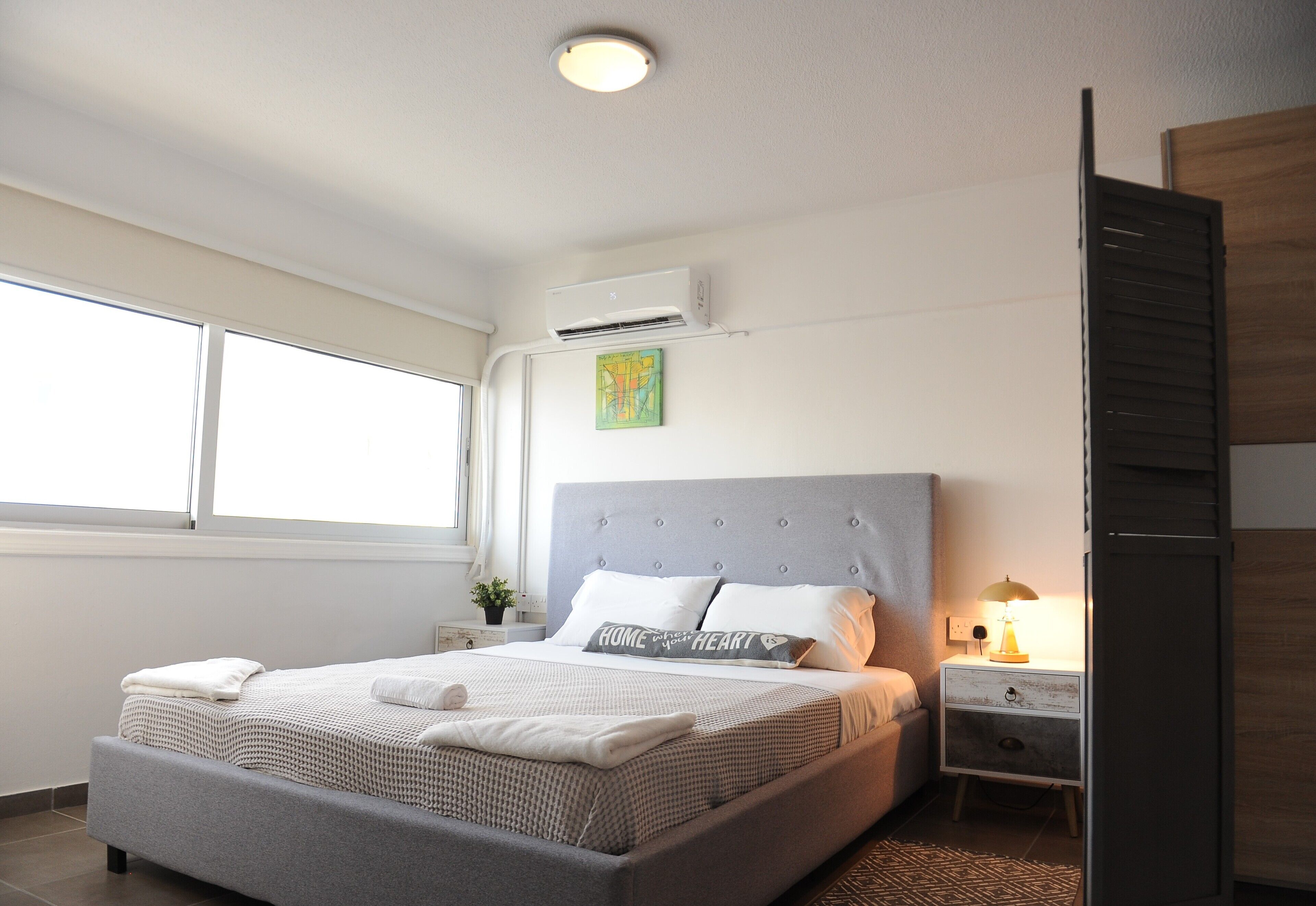 A modern bedroom with a large bed, a bedside table with a lamp, and a window with curtains.