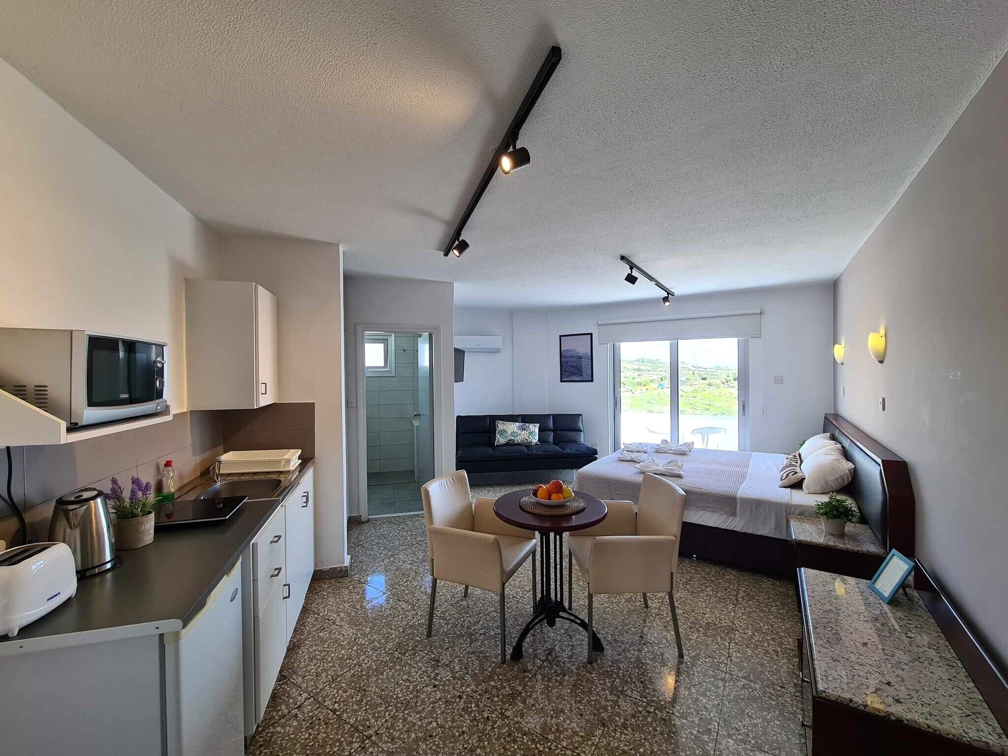 Habitación de hotel moderna con kitchenette, zona de comedor, cama y vistas al exterior.