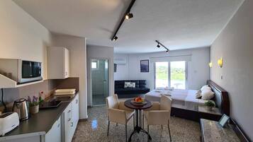 Habitación de hotel moderna con kitchenette, zona de comedor, cama y vistas al exterior.