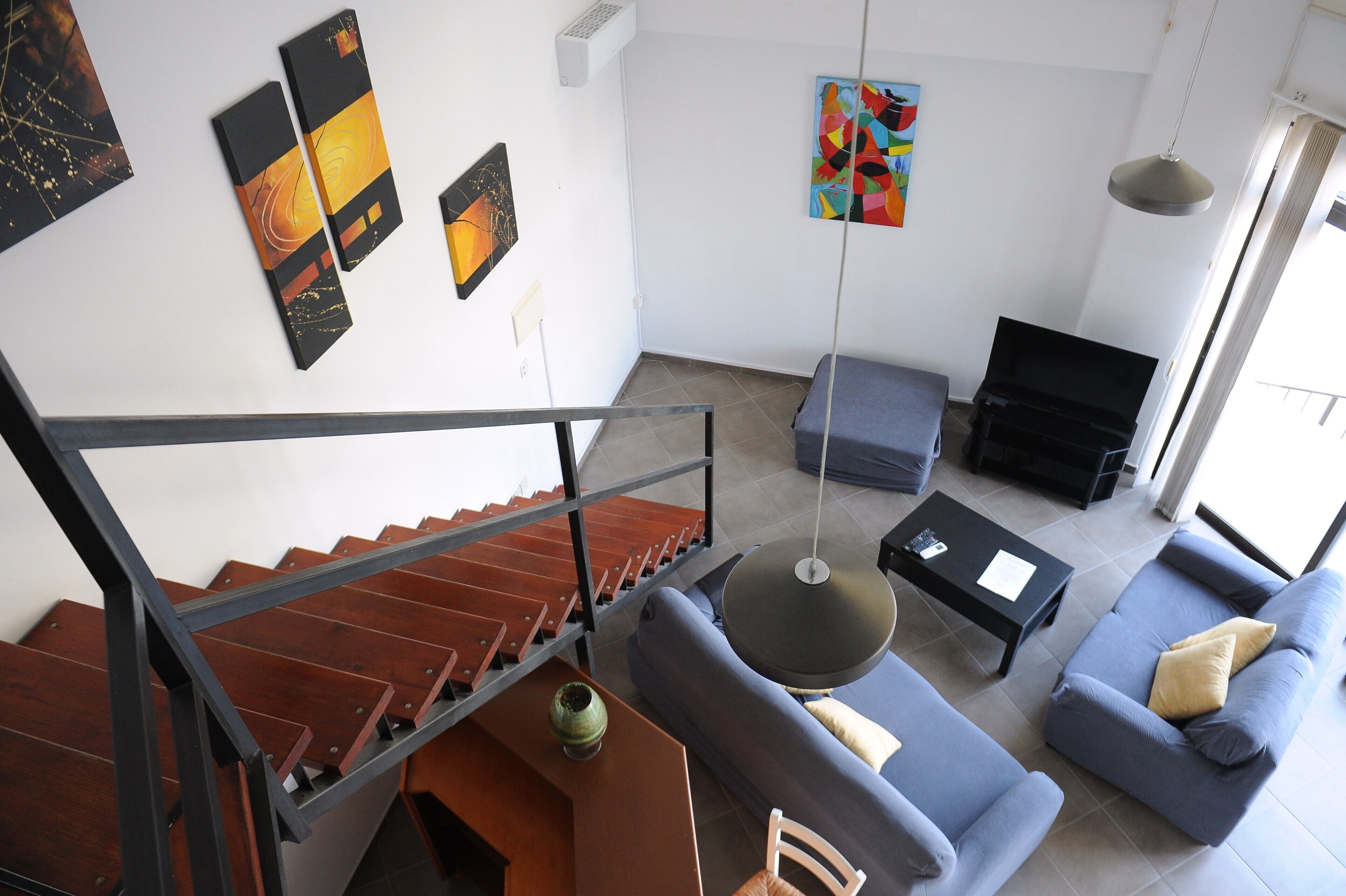 A modern living room with a staircase, a sofa set, a coffee table, and artwork on the walls.