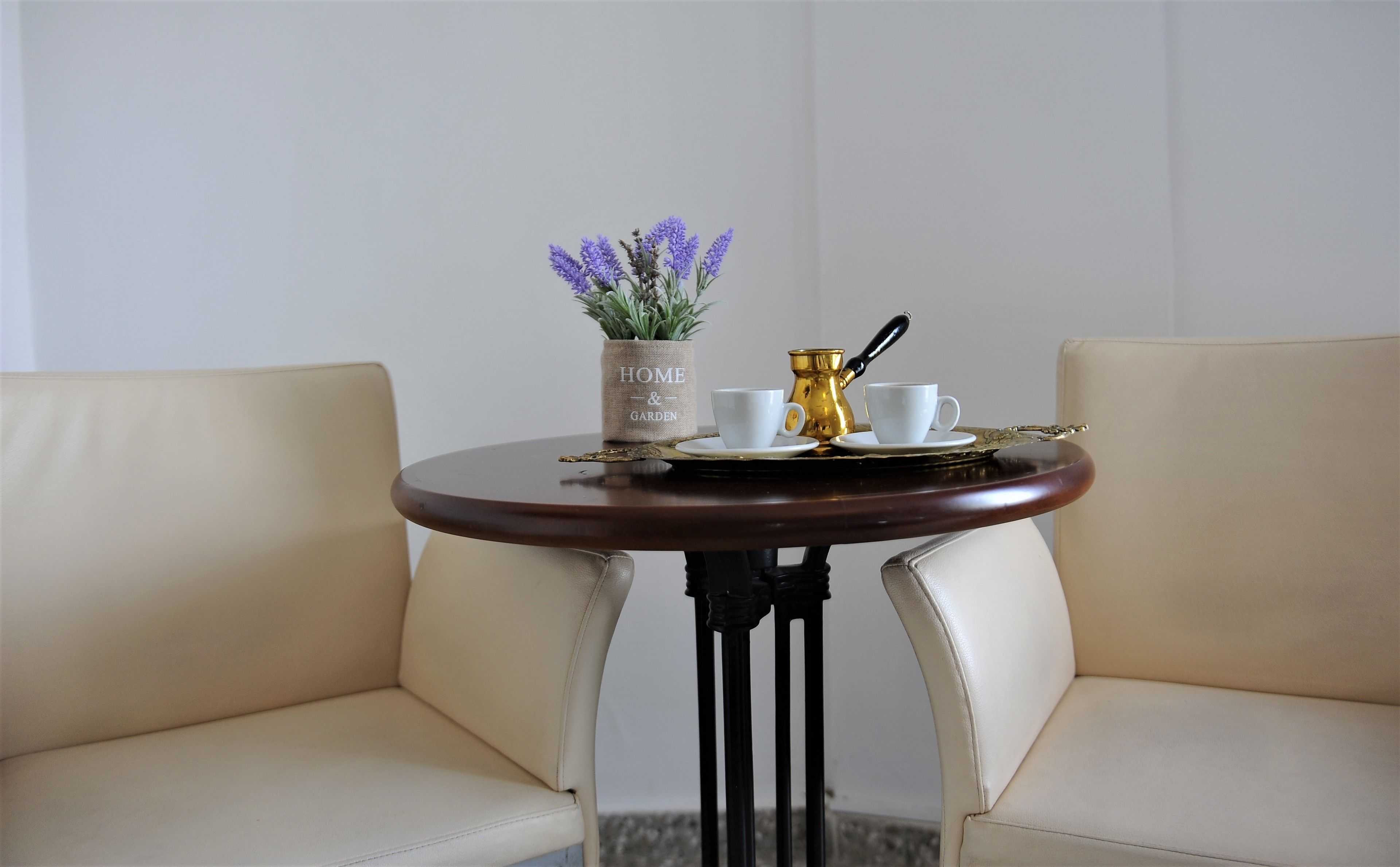 A small round table with a vase of purple flowers, two white cups, and a gold teapot on a tray.