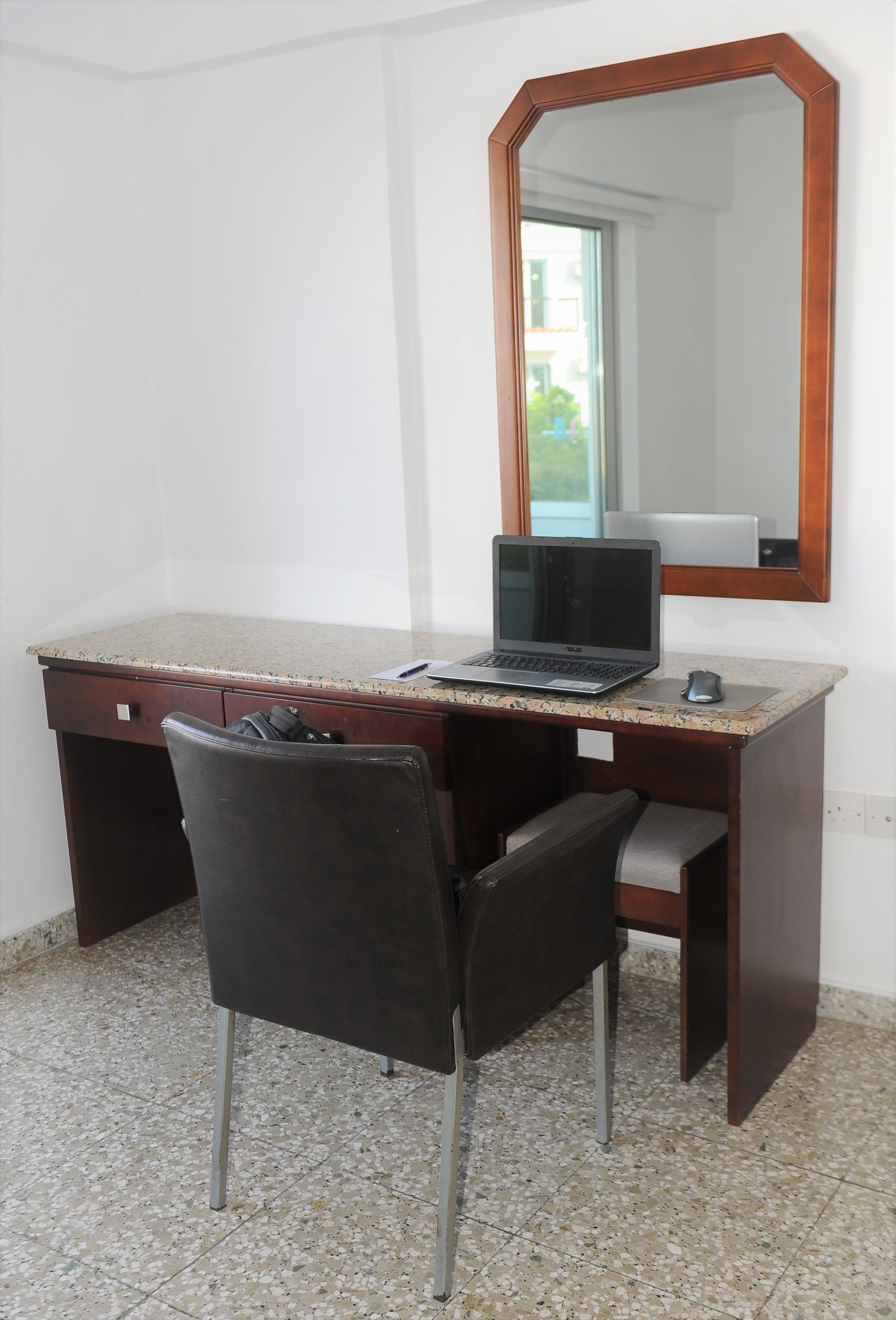 A small office space with a desk, chair, laptop, and a mirror.