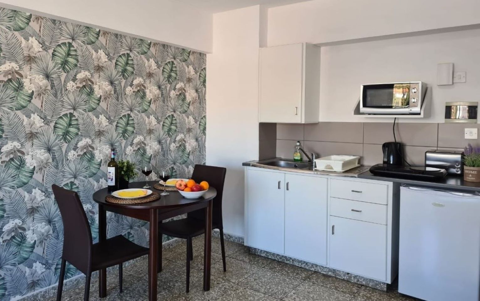 A compact kitchen with white cabinets, a microwave, and a small dining area with a table and chairs.