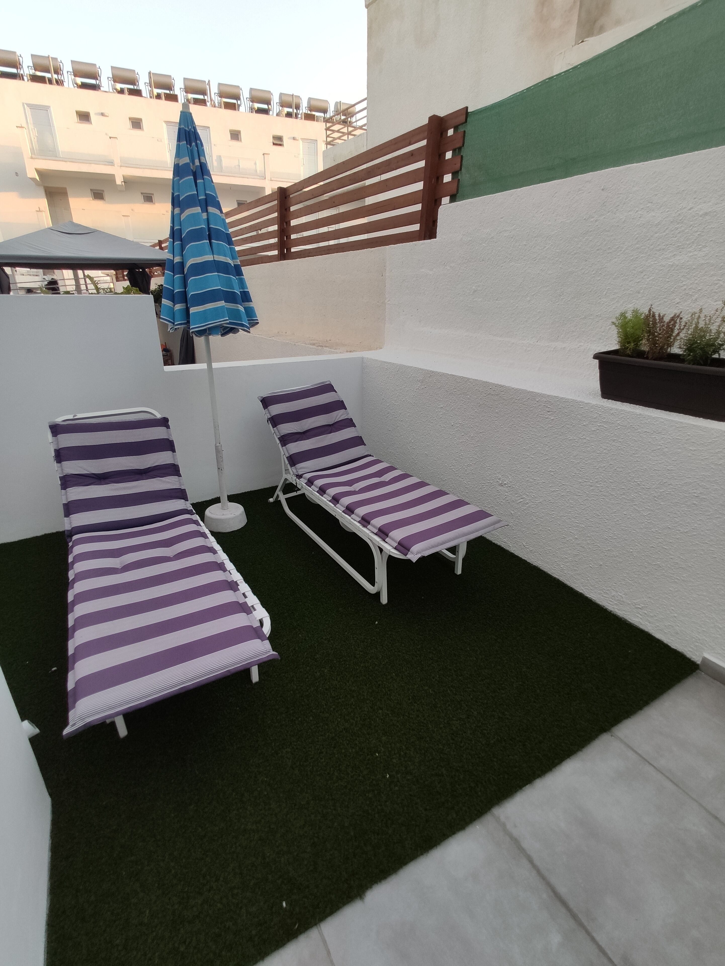 Una terraza en la azotea con dos sillones de exterior a rayas y un parasol azul con rayas.