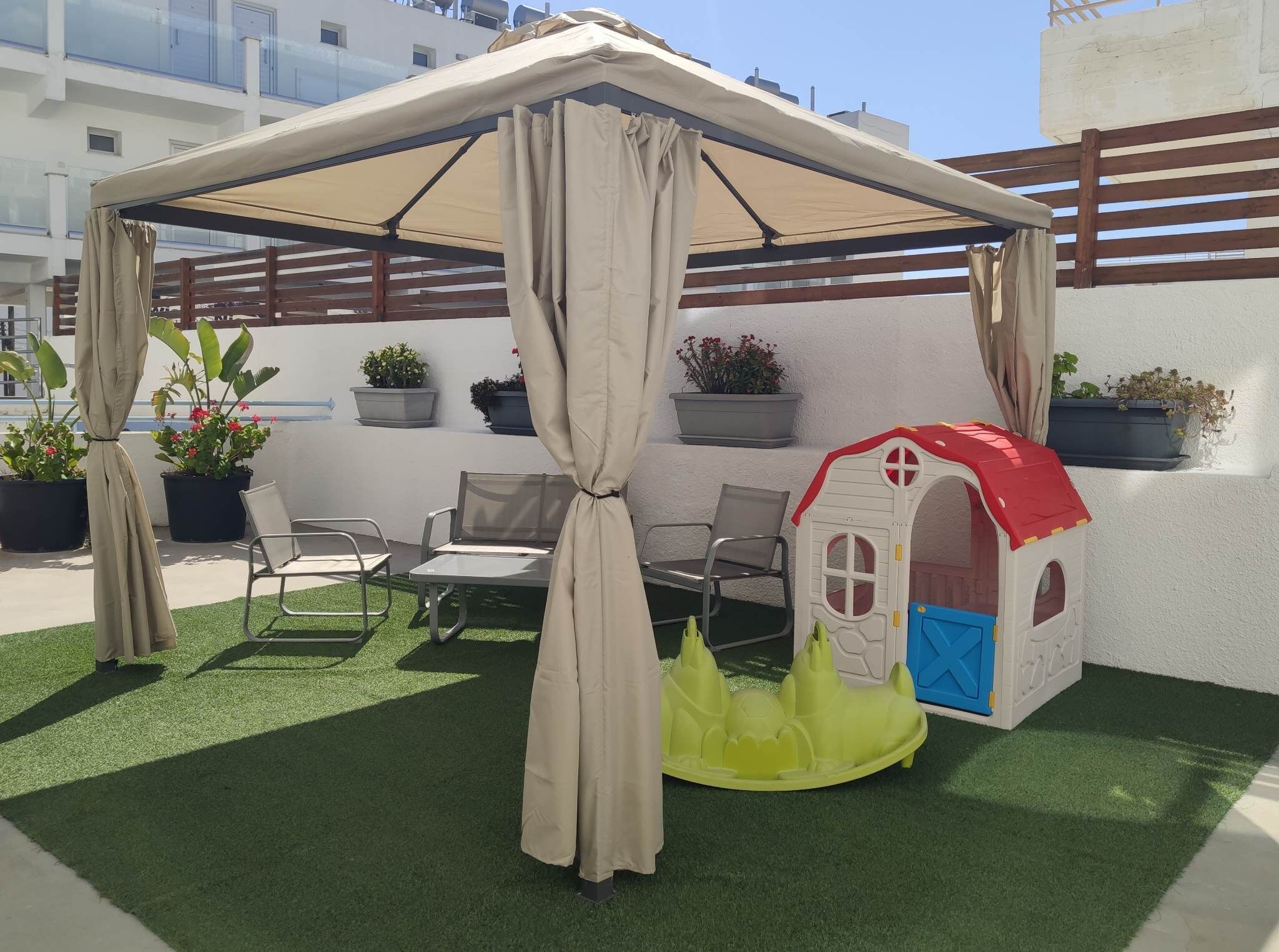 A covered patio with a playhouse, chairs, and potted plants.