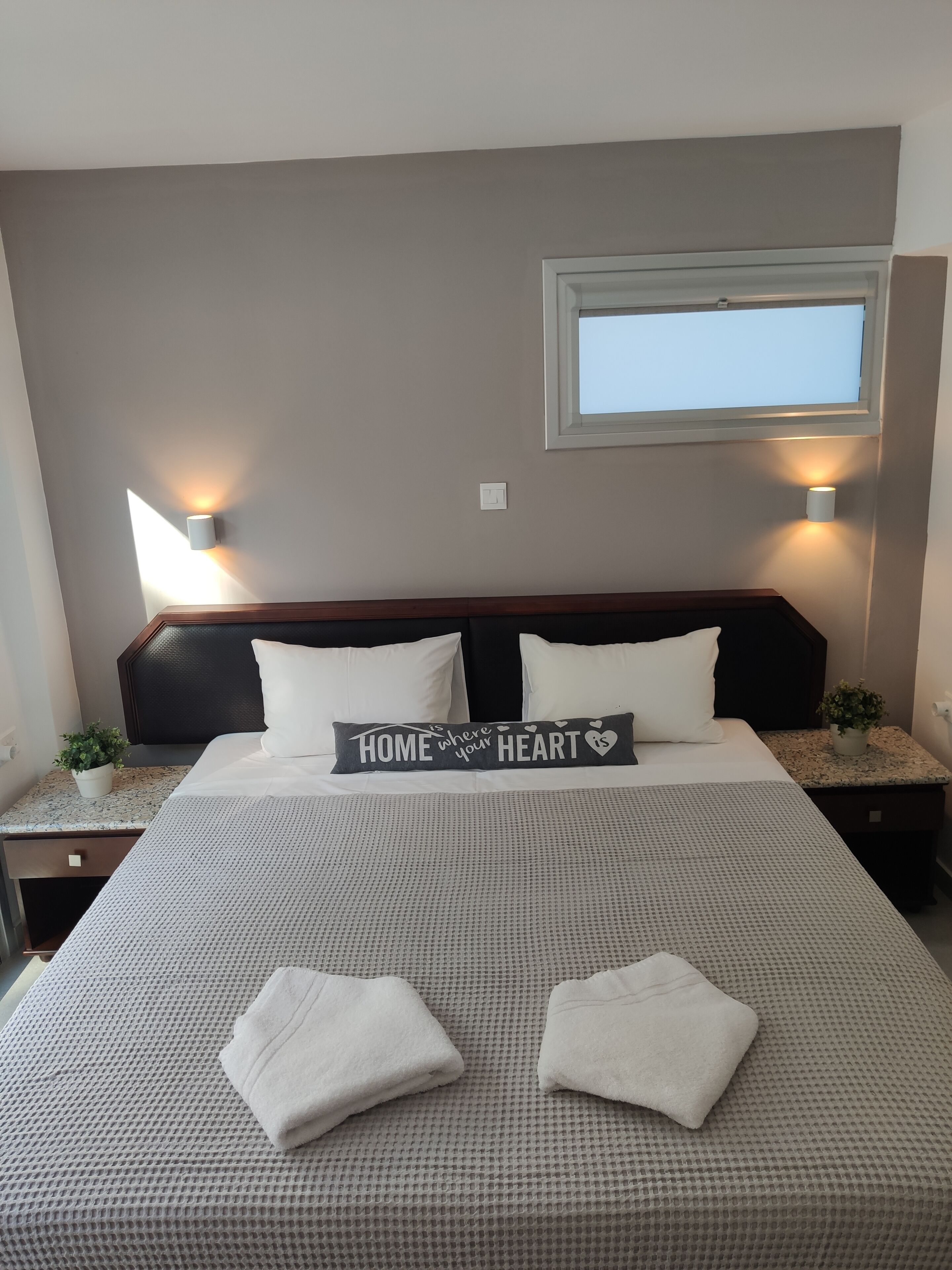 A neatly made bed with a decorative pillow, bedside tables with lamps, and a window above the bed.