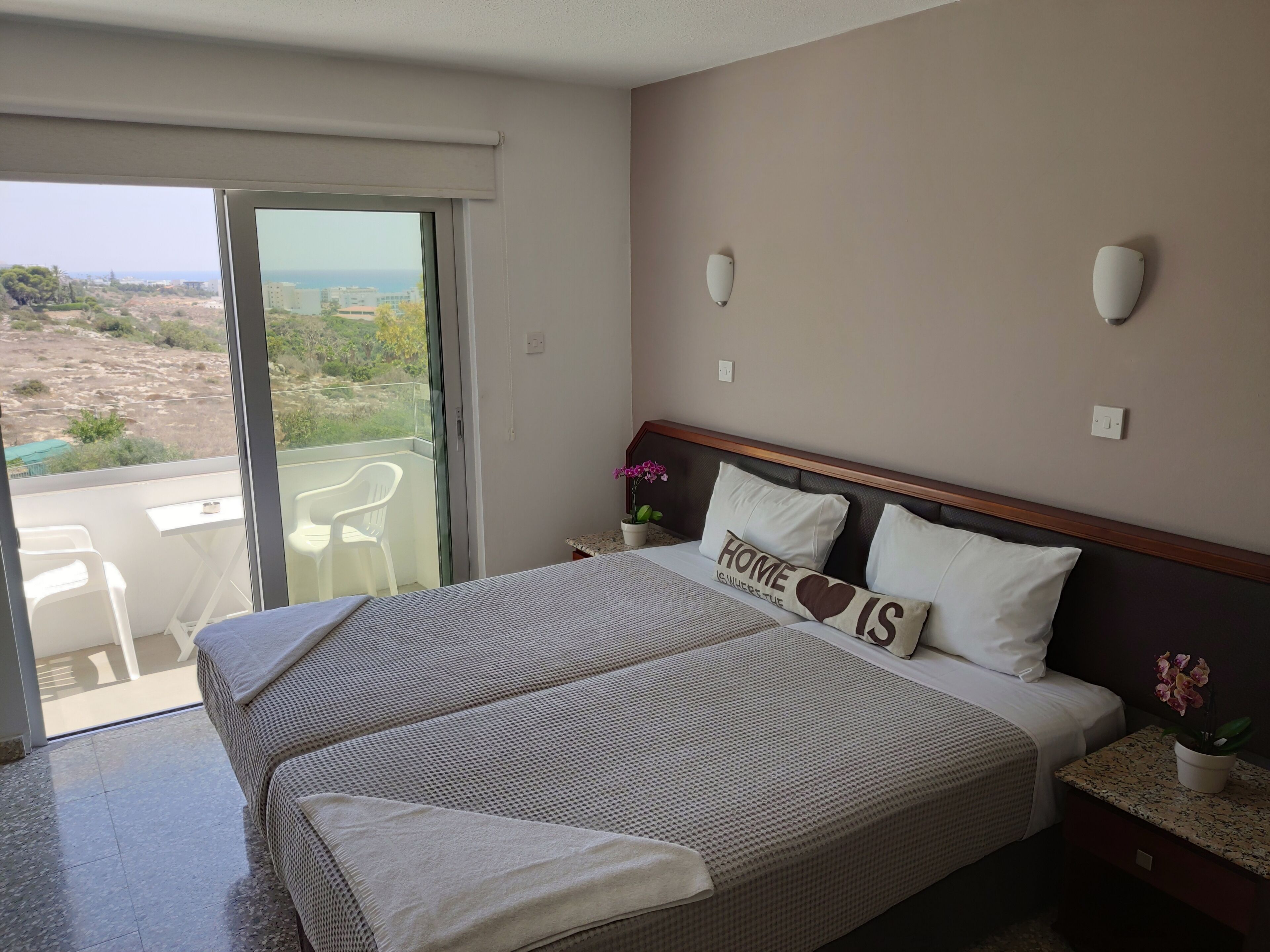 A hotel room with a large bed, a balcony with a view of the landscape, a small table, and a chair.