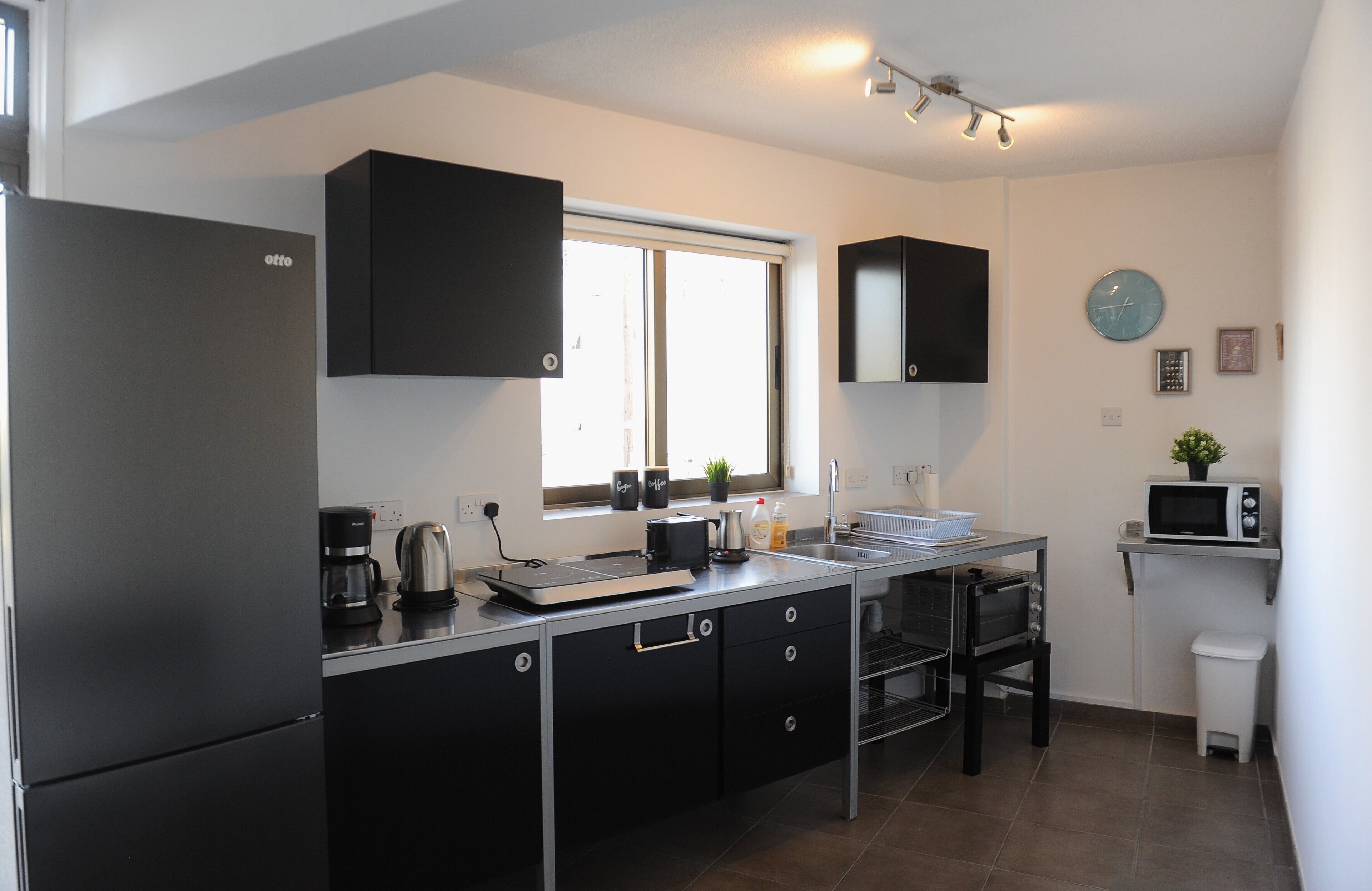 A modern kitchen with a refrigerator, coffee maker, kettle, toaster, and microwave.
