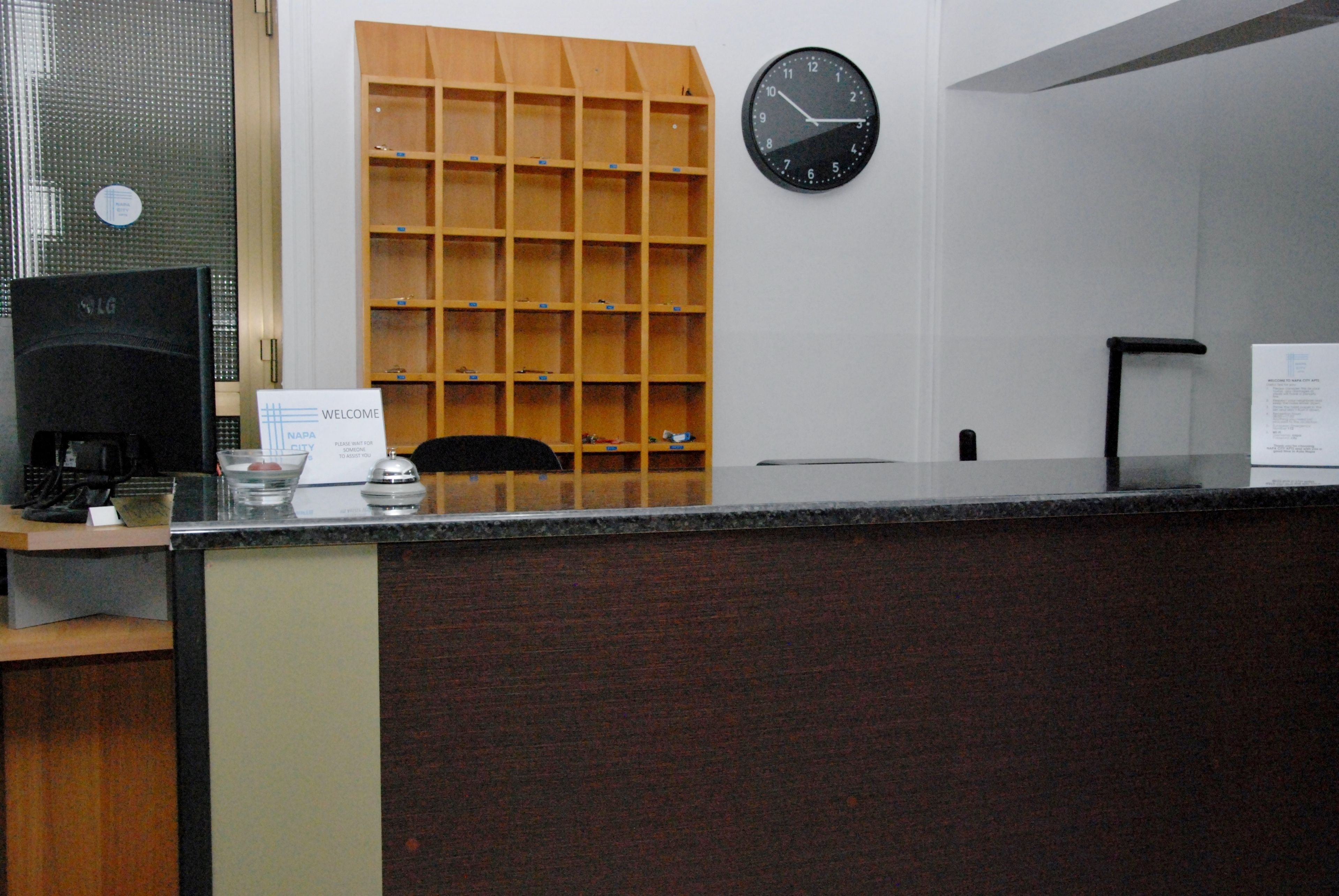 A reception desk with a clock, a welcome sign, and a wooden shelf unit.