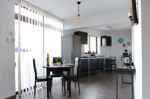 A modern kitchen with a dining area, featuring a refrigerator, sink, and a coffee machine. - Napa City Apartments (Ayia Napa)