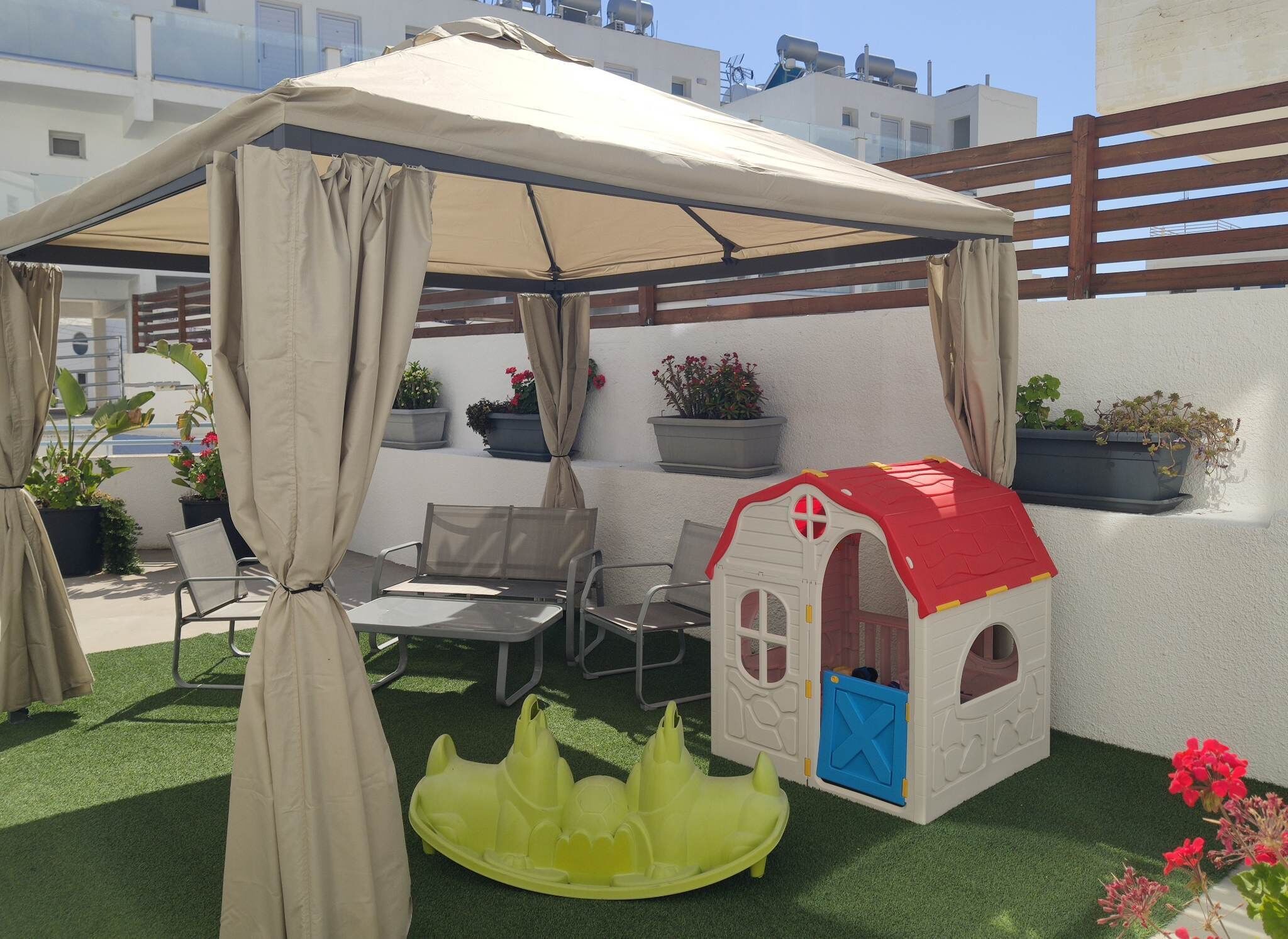 A covered patio area with a playhouse, artificial turf, and potted plants.