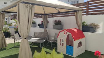 A covered patio area with a playhouse, artificial turf, and potted plants.