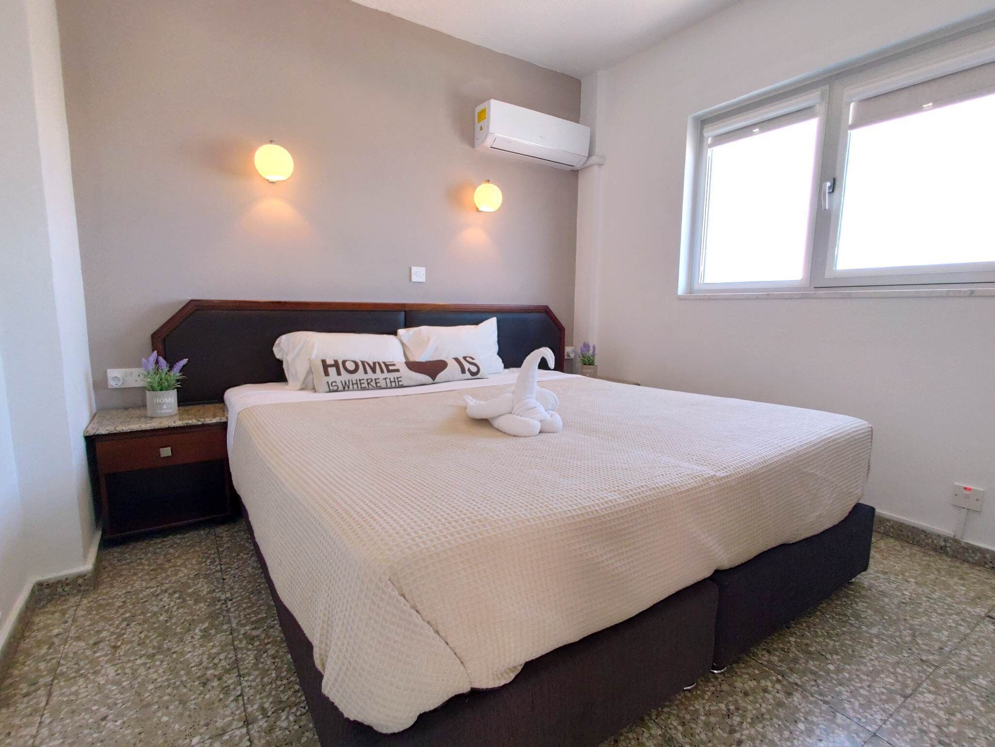 A bedroom with a bed, a nightstand, a wall-mounted air conditioner, and a window.