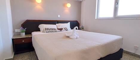 A bedroom with a bed, a nightstand, a wall-mounted air conditioner, and a window.
