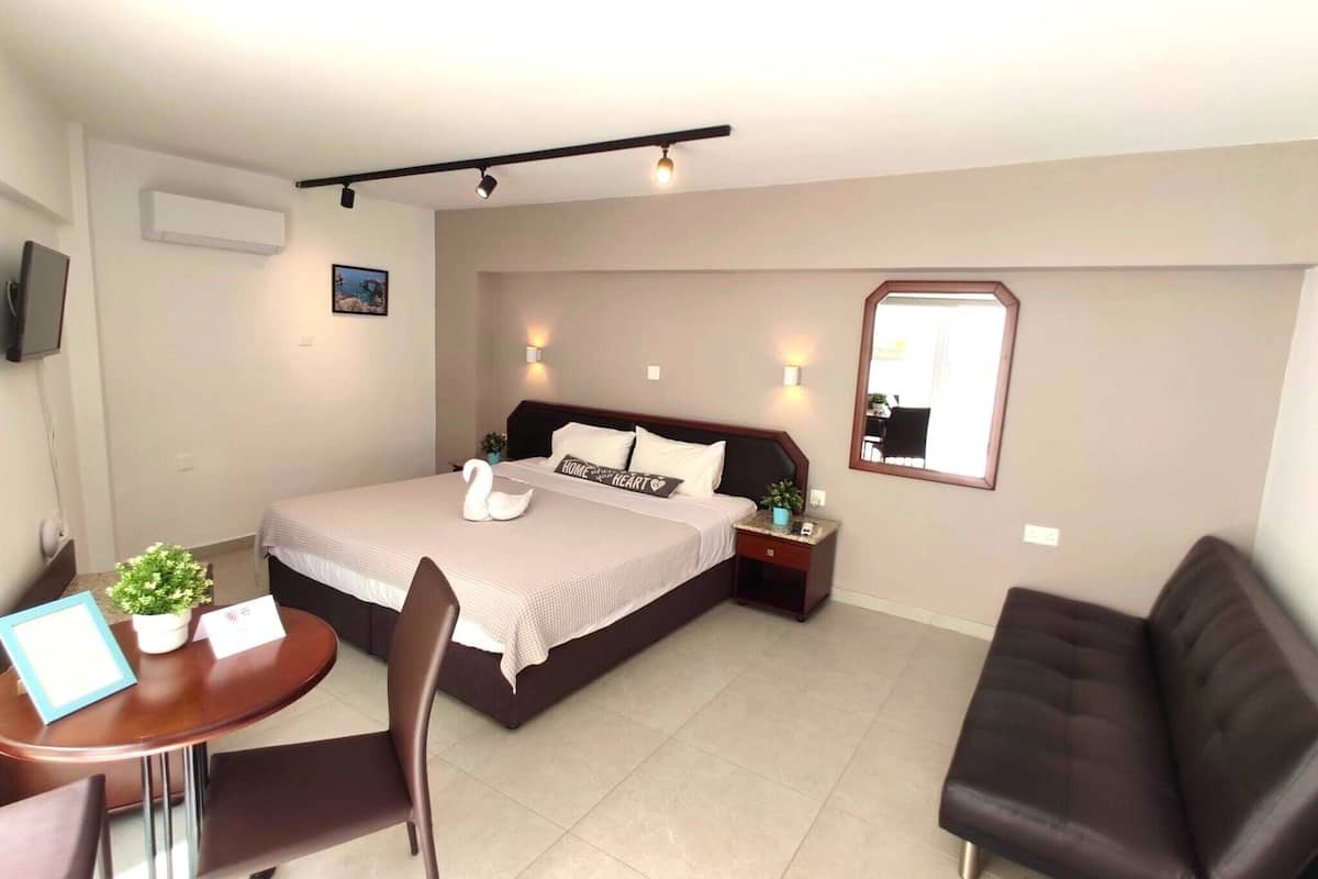 Habitación de hotel con cama, escritorio con silla, una mesita con planta y espejo en la pared.