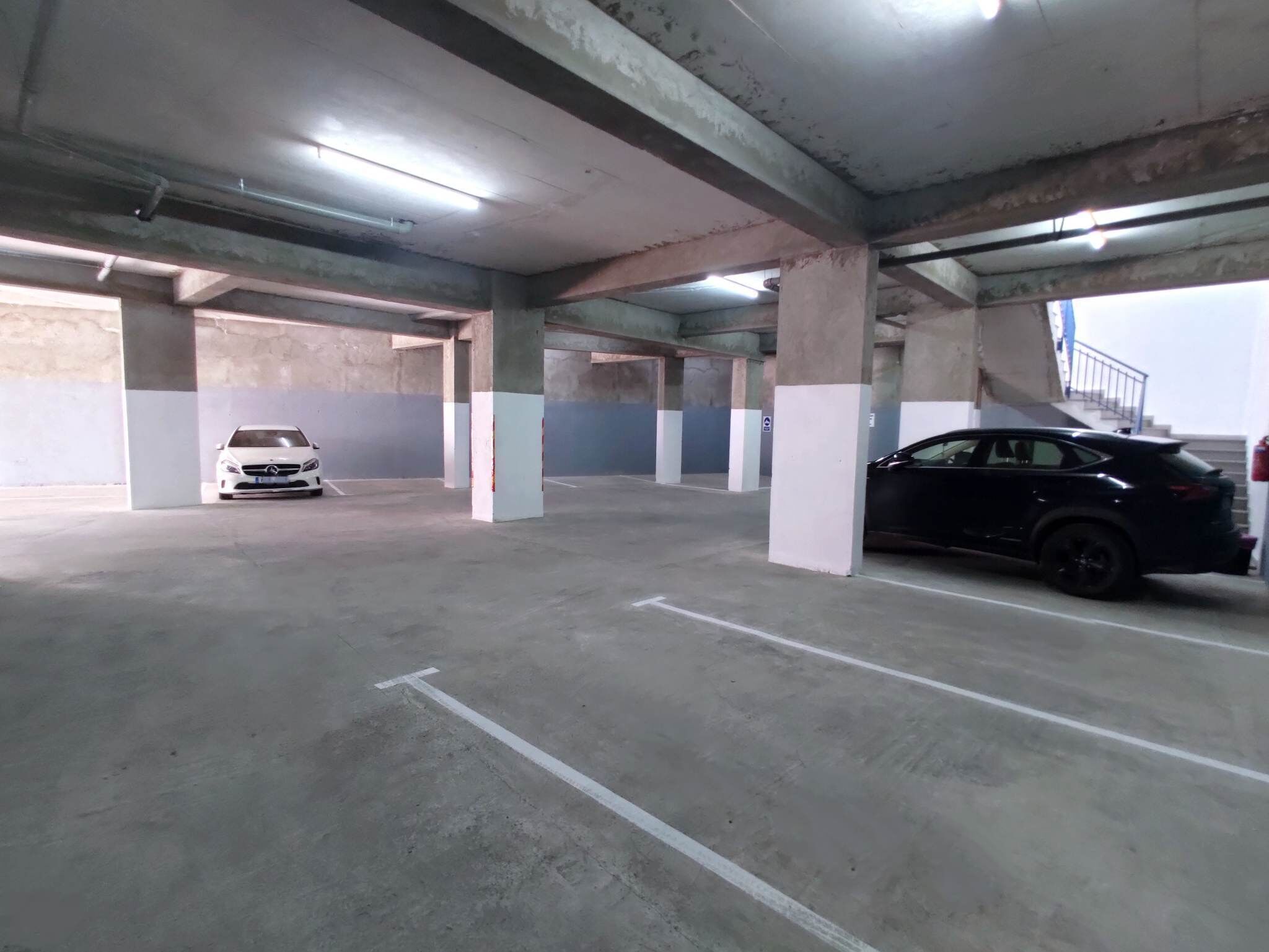 Un estacionamiento con varios niveles, pilares de concreto y paredes blancas y grises.