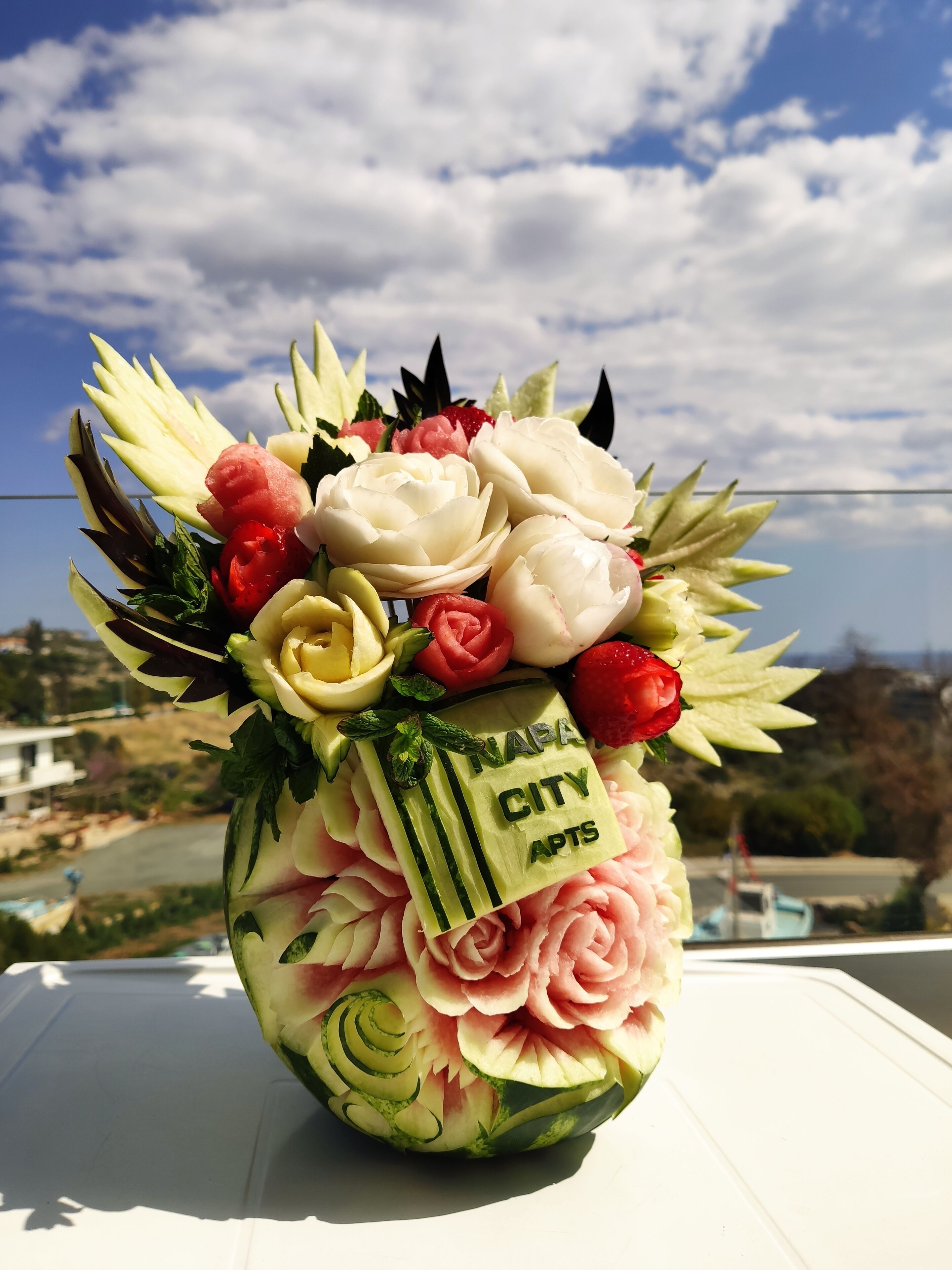A watermelon carved into a floral arrangement with text reading "NAPA CITY APTS".