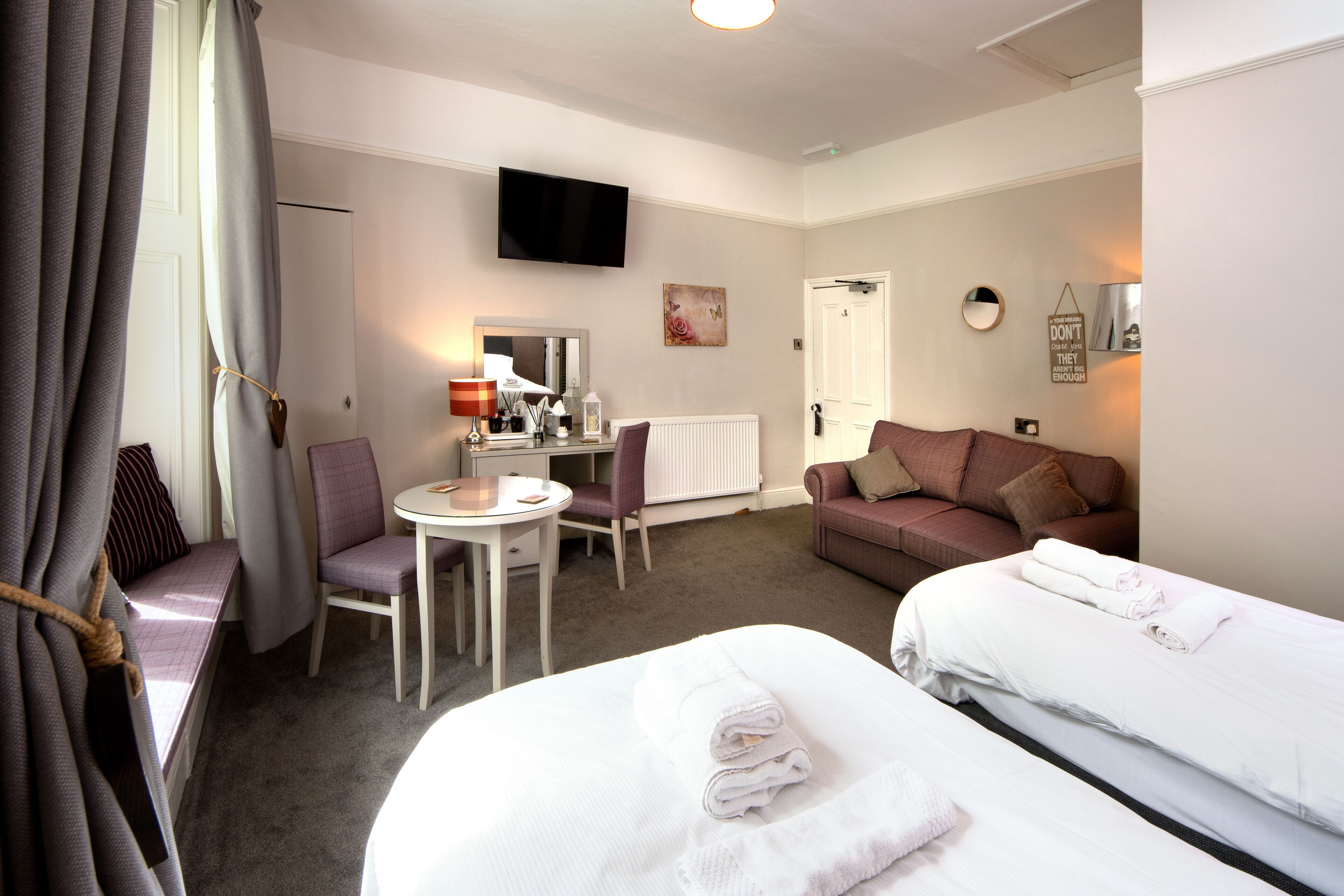 A hotel room with two beds, a desk, a chair, a TV, and a window with curtains.