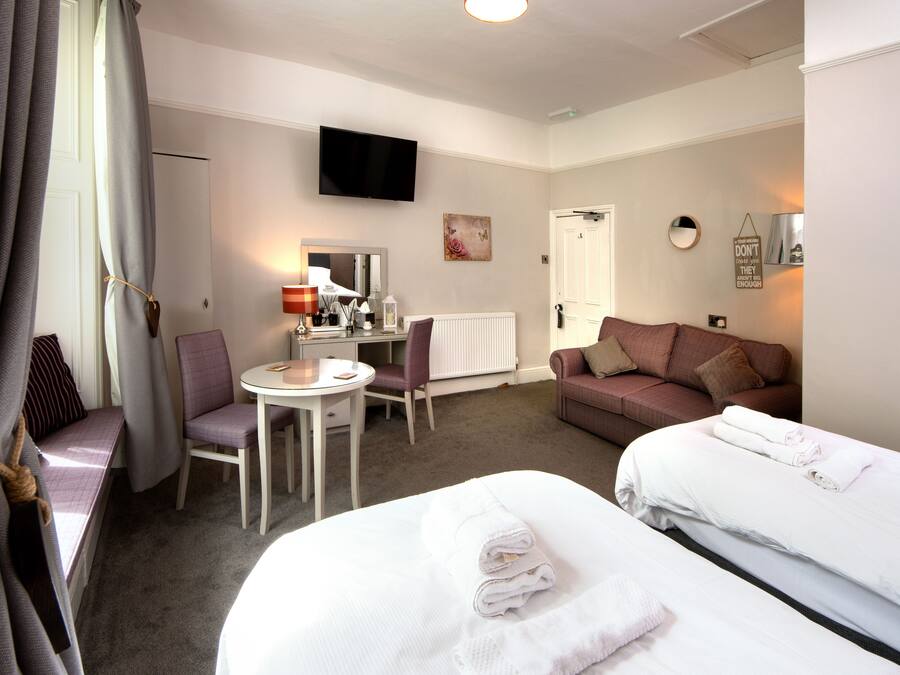 A hotel room with two beds, a desk, a chair, a TV, and a window with curtains.