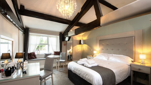 A hotel room with a large bed, a desk with a chair, a small table, and a chandelier. - Maypole Inn (Skipton)