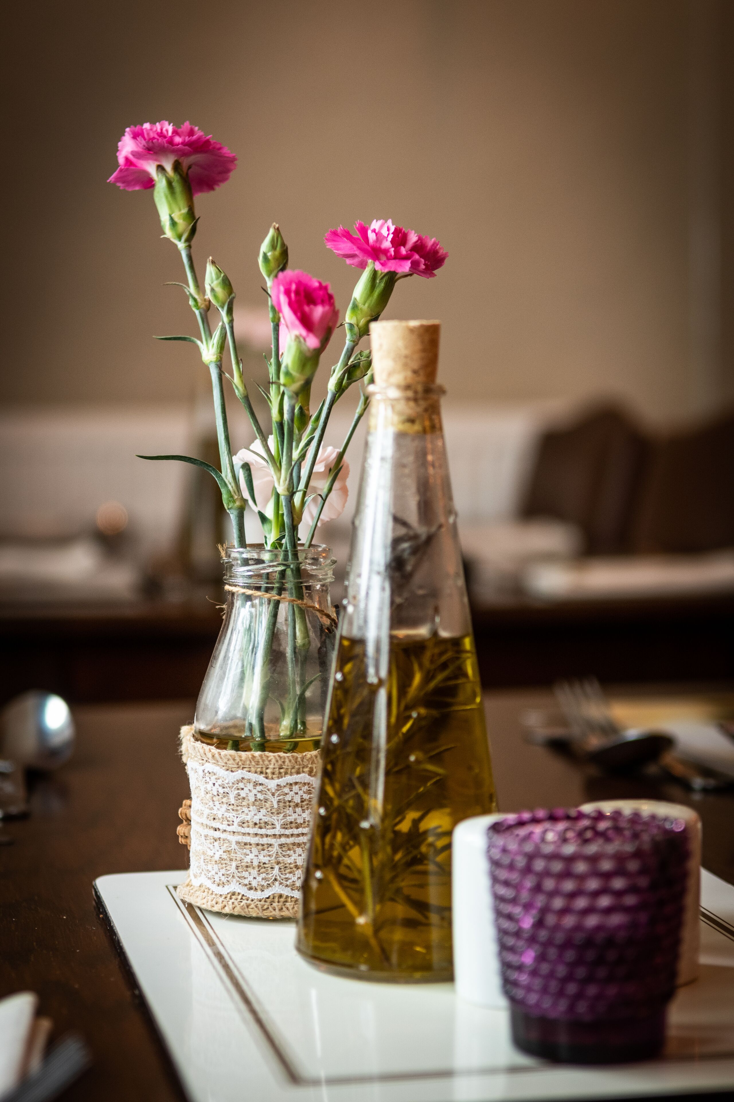 Una mesa con una botella de vidrio, un tarro con flores y una taza morada.
