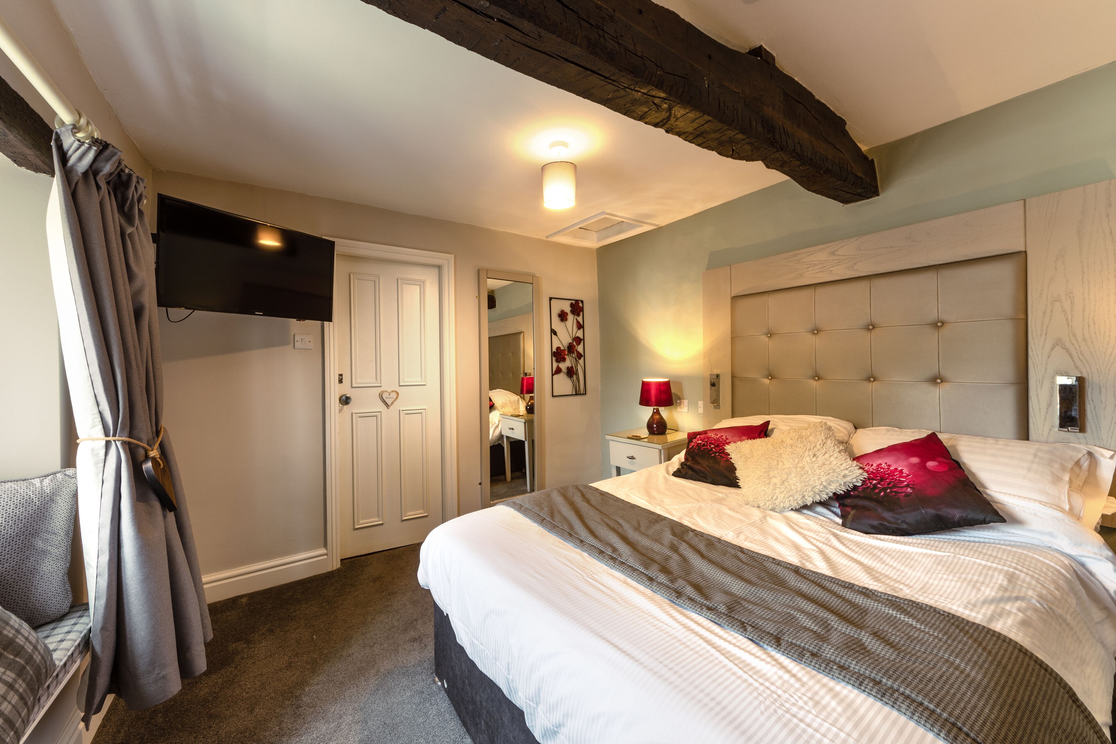 A bedroom with a bed, bedside table, lamp, and a television mounted on the wall.