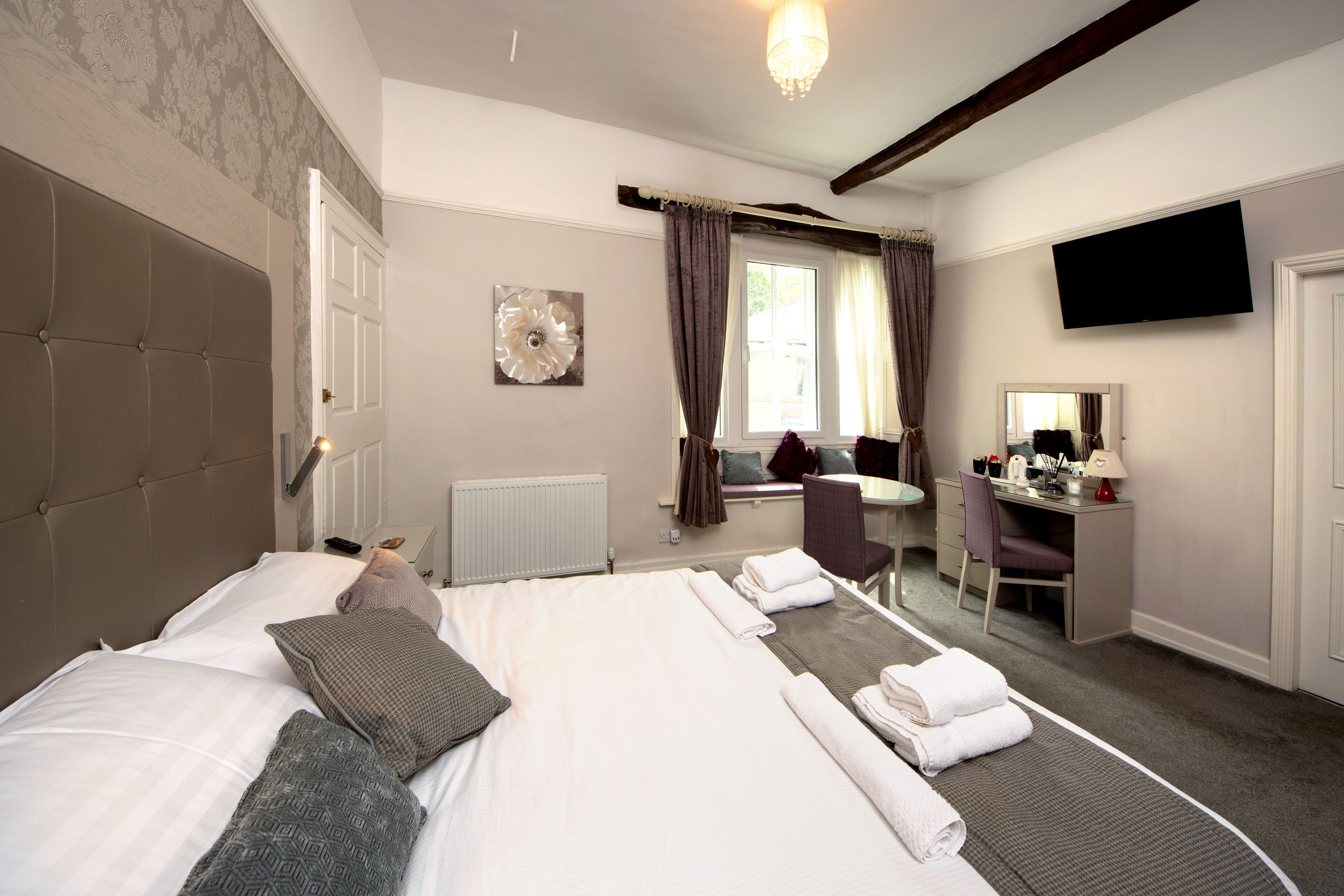 A hotel room with a large bed, a desk, a chair, a flat-screen TV, and a window with curtains.