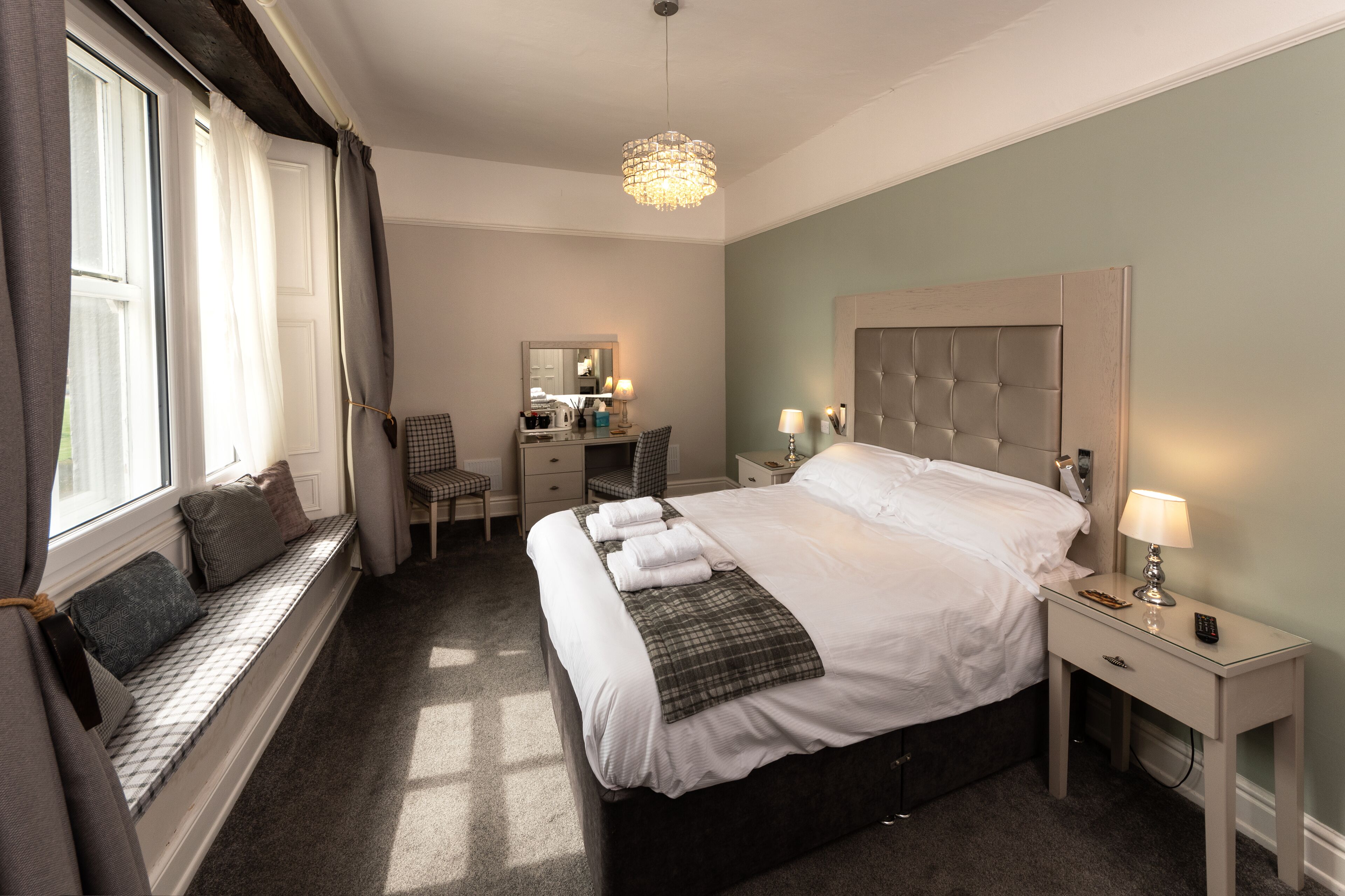 Een slaapkamer met een groot bed, een nachtkastje met een lamp, een stoel, een bureau en een raam met gordijnen.