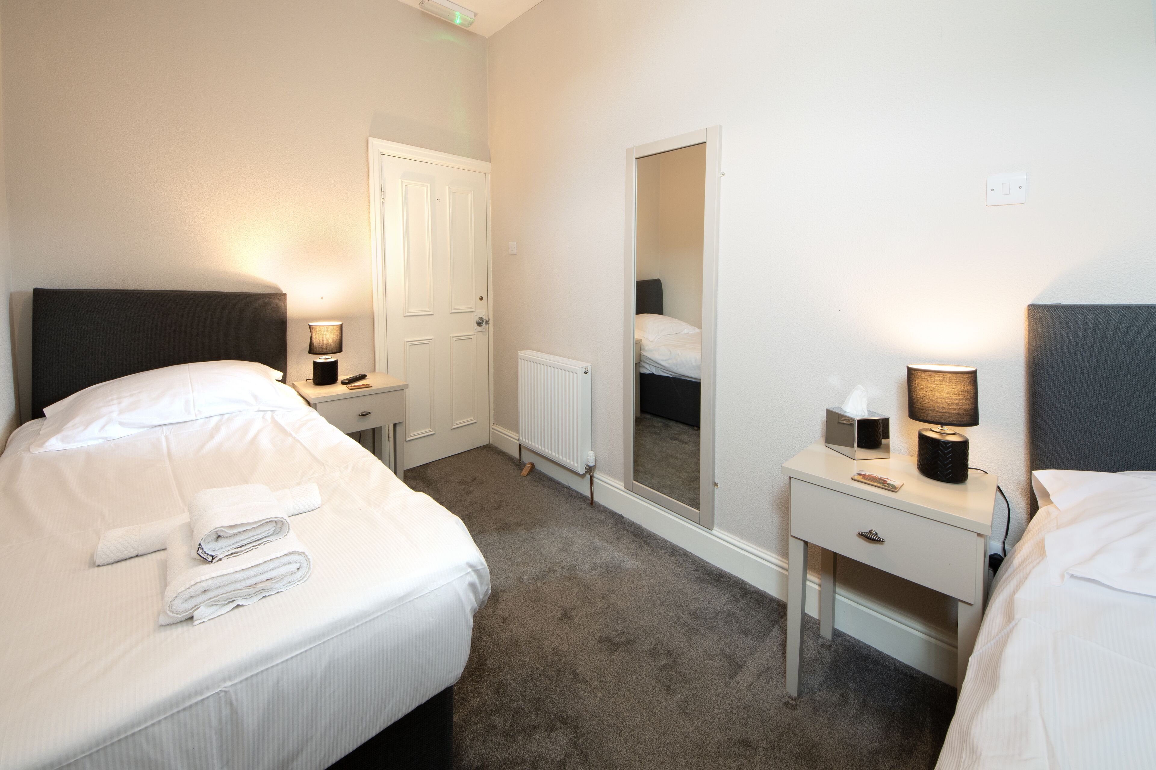 Ein Hotelzimmer mit Bett, Nachttisch, Lampe und Spiegel.