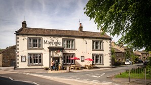 A two-story building named 'The Maypole' with a traditional architectural style, featuring a signboard, windows, and outdoor seating area with red umbrellas. - Maypole Inn (Skipton)