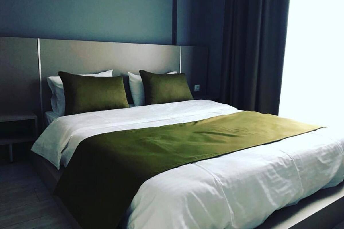 Una cama bien tendida con una colcha blanca y verde, cabecera gris y dos almohadas.