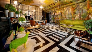 Un hall d’hôtel moderne avec un sol à carreaux, un canapé vert et une fresque représentant une forêt.
