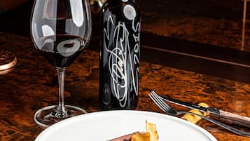 Un plato con carne, papas fritas, una copa de vino y una botella de vino sobre una mesa de madera.